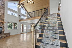 Stairs featuring hardwood / wood-style flooring, a stone fireplace, beamed ceiling, a ceiling fan, and high vaulted ceiling
