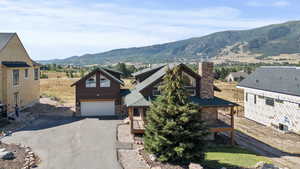 View of front facade featuring a chimney, a mountain view, asphalt driveway, an attached garage, and stone siding