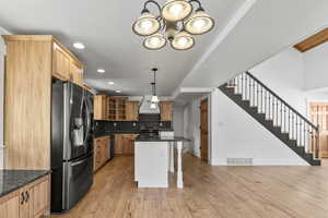 Kitchen with a kitchen bar, stainless steel appliances, glass insert cabinets, decorative light fixtures, and light wood-type flooring