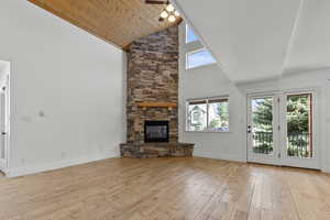 Unfurnished living room featuring light wood-type flooring, high vaulted ceiling, a stone fireplace, and wood ceiling