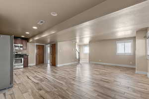 Kitchen featuring appliances with stainless steel finishes, dark countertops, open floor plan, light wood-type flooring, and recessed lighting