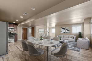 Staged basement great room with kitchen, dining and living room featuring light wood-type flooring and recessed lighting
