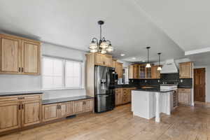 Kitchen with stainless steel refrigerator with ice dispenser, premium range hood, dark stone countertops, backsplash, and hanging light fixtures