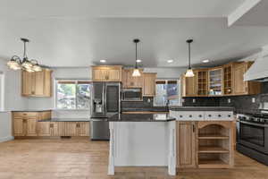 Kitchen featuring appliances with stainless steel finishes, hanging light fixtures, dark countertops, tasteful backsplash, and light wood-type flooring