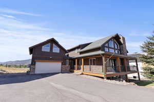 View of front of home with board and batten siding, a garage, asphalt driveway, a porch, and a chimney