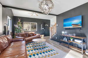 Living area featuring beam ceiling, stairs, wood finished floors, ceiling fan, and a chandelier