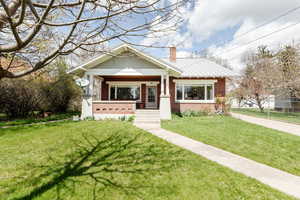 View of front of house featuring brick siding, a porch, a front lawn, and a chimney