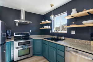 Kitchen featuring blue cabinets, stainless steel appliances, wall chimney exhaust hood, and open shelves