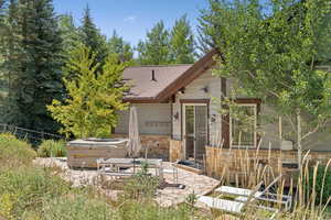 Rear view of house featuring a hot tub, stone siding, a patio, and roof with shingles