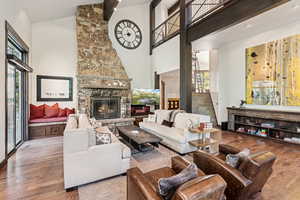 Living room with hardwood / wood-style flooring, a stone fireplace, stairs, and high vaulted ceiling