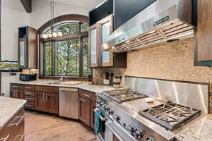 Kitchen featuring ventilation hood, stainless steel appliances, light stone countertops, backsplash, and light wood finished floors