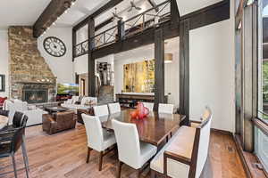Dining space featuring wood-type flooring, a stone fireplace, healthy amount of natural light, beamed ceiling, and a towering ceiling