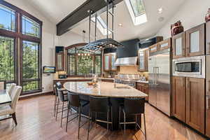 Kitchen featuring glass insert cabinets, tasteful backsplash, a skylight, a kitchen island with sink, and built in appliances