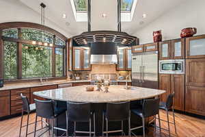 Kitchen with tasteful backsplash, glass insert cabinets, vaulted ceiling, a breakfast bar area, and light wood-style floors