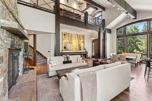 Living area featuring a stone fireplace, hardwood / wood-style flooring, beamed ceiling, high vaulted ceiling, and stairs