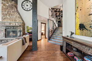 Living room featuring wood-type flooring, a stone fireplace, high vaulted ceiling, and stairway