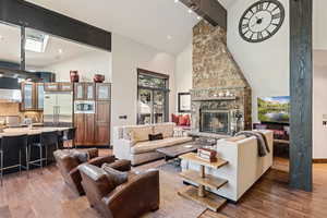 Living area featuring beam ceiling, light wood-style flooring, a stone fireplace, a skylight, and high vaulted ceiling