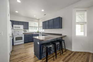 Kitchen with blue cabinetry, a kitchen breakfast bar, white appliances, dark countertops, and a peninsula