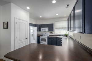 Kitchen featuring white appliances, dark countertops, a peninsula, and recessed lighting