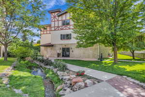 Rear view of house featuring a lawn, stucco siding, and stone siding