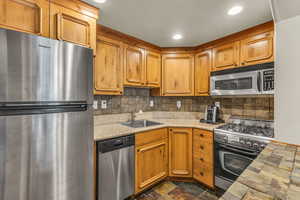 Kitchen featuring stainless steel appliances, decorative backsplash, dark stone finish flooring, brown cabinets, and recessed lighting
