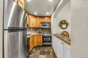 Kitchen featuring appliances with stainless steel finishes, dark stone finish flooring, recessed lighting, decorative backsplash, and brown cabinets