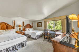 Bedroom featuring light colored carpet, vaulted ceiling, and a desk