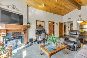 Carpeted living area with high vaulted ceiling, a wood ceiling with exposed beams, and a tile fireplace