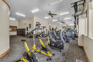 Gym with a ceiling fan, a textured ceiling, and dark colored carpet