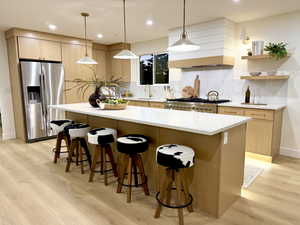 Kitchen with stainless steel appliances, pendant lighting, light wood-style flooring, light brown cabinets, and decorative backsplash