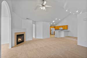 Unfurnished living room with light carpet, vaulted ceiling, a tiled fireplace, a ceiling fan, and recessed lighting