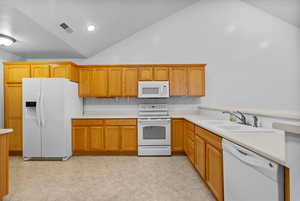 Kitchen featuring white appliances, light countertops, vaulted ceiling, and a peninsula