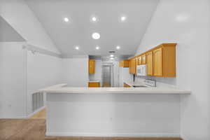 Kitchen featuring vaulted ceiling, light countertops, light colored carpet, a peninsula, and white appliances