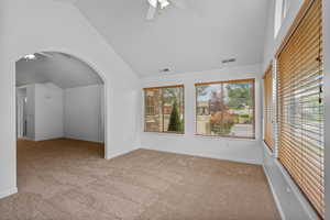 Empty room featuring ceiling fan, lofted ceiling, light carpet, and arched walkways