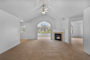 Unfurnished living room with vaulted ceiling, light carpet, a tile fireplace, and ceiling fan