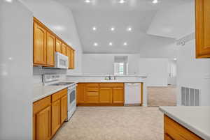 Kitchen with white appliances, light countertops, a peninsula, recessed lighting, and high vaulted ceiling