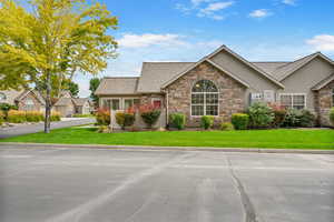 View of front of property featuring a front yard, stone siding, stucco siding, and a shingled roof