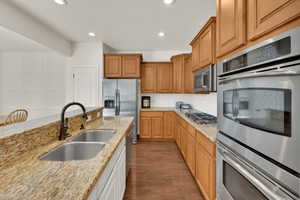 Kitchen with appliances with stainless steel finishes, recessed lighting, light stone counters, tasteful backsplash, and dark wood-type flooring