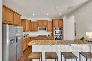 Kitchen with stainless steel appliances, light stone countertops, decorative backsplash, recessed lighting, and dark wood-style floors