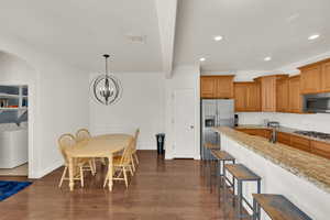 Kitchen with brown cabinetry, washer / clothes dryer, light stone countertops, dark wood-type flooring, and stainless steel appliances