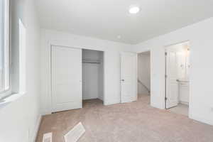 Unfurnished bedroom featuring light carpet, a closet, and ensuite bathroom