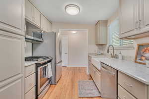 Kitchen featuring appliances with stainless steel finishes, light wood-style flooring, light stone countertops, and tasteful backsplash
