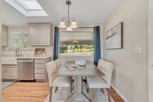 Dining room with light wood-style floors, a skylight, and a chandelier