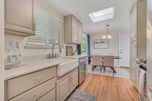 Kitchen featuring a skylight, backsplash, light stone counters, light wood-style flooring, and a chandelier