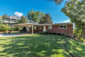 Ranch-style home featuring brick siding, a front yard, a carport, driveway, and a porch