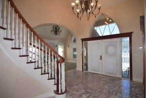 Foyer with french doors, a chandelier, plenty of natural light, a towering ceiling, and arched walkways