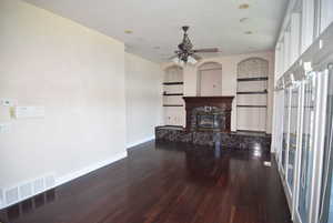 Living area featuring built in features, dark wood-type flooring, a high end fireplace, and a ceiling fan
