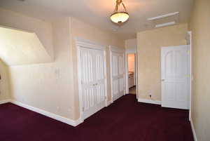 Additional living space featuring attic access and dark colored carpet