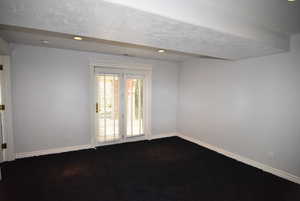 Empty room with a textured ceiling, recessed lighting, and dark carpet
