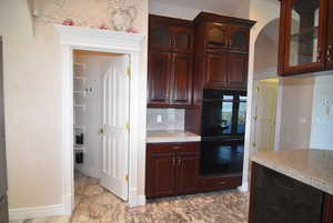 Kitchen featuring glass insert cabinets, tile counters, dark brown cabinetry, tasteful backsplash, and arched walkways